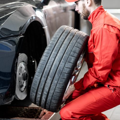Car service worker in red uniform changing wheel of a sport car at the tire mounting service